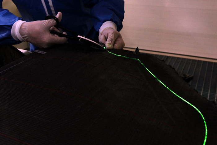 利用激光在一片碳化纤维上绘出一条切口线之后，工厂师傅手工沿切口线将其切开